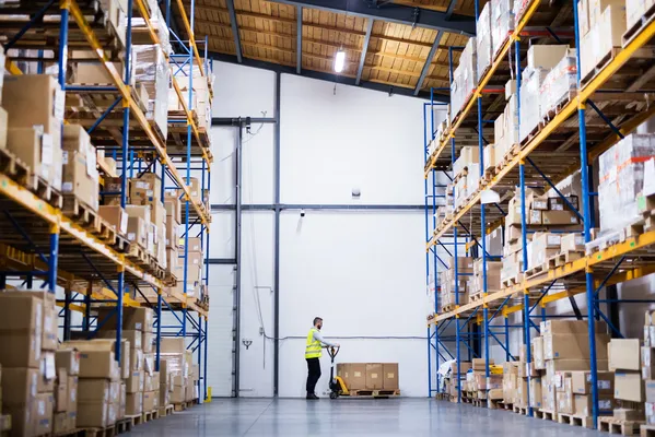 Employees check the arrangement of boxes on high shelves, ensuring proper product management within a bonded warehouse.