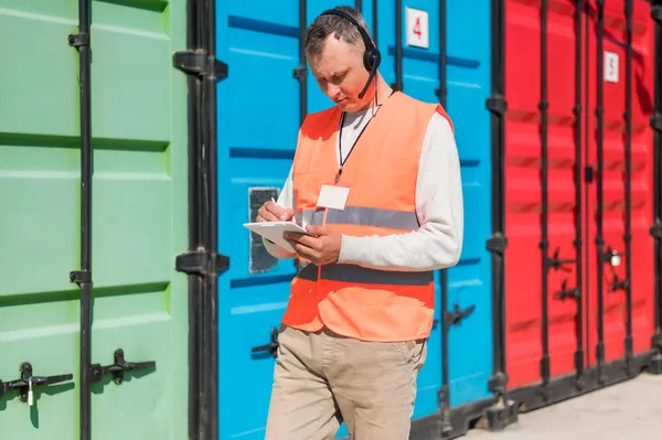 A worker with a vest and portable radio takes notes in front of containers, evoking the document control carried out by a Customs broker Laredo TX.
